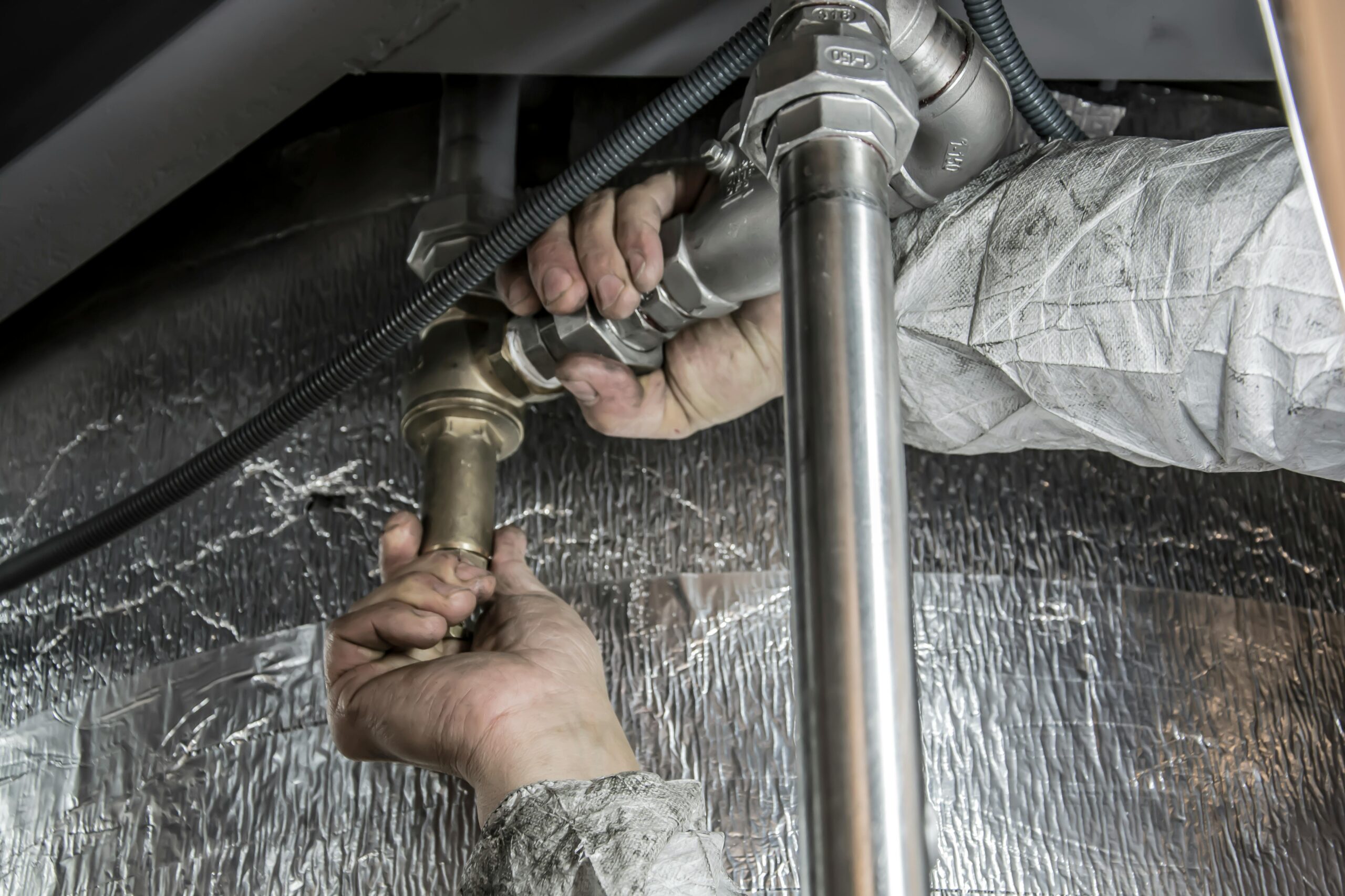 Rørlegger monterer og strammer koblinger på vannrør under installasjon av VVS-system.
